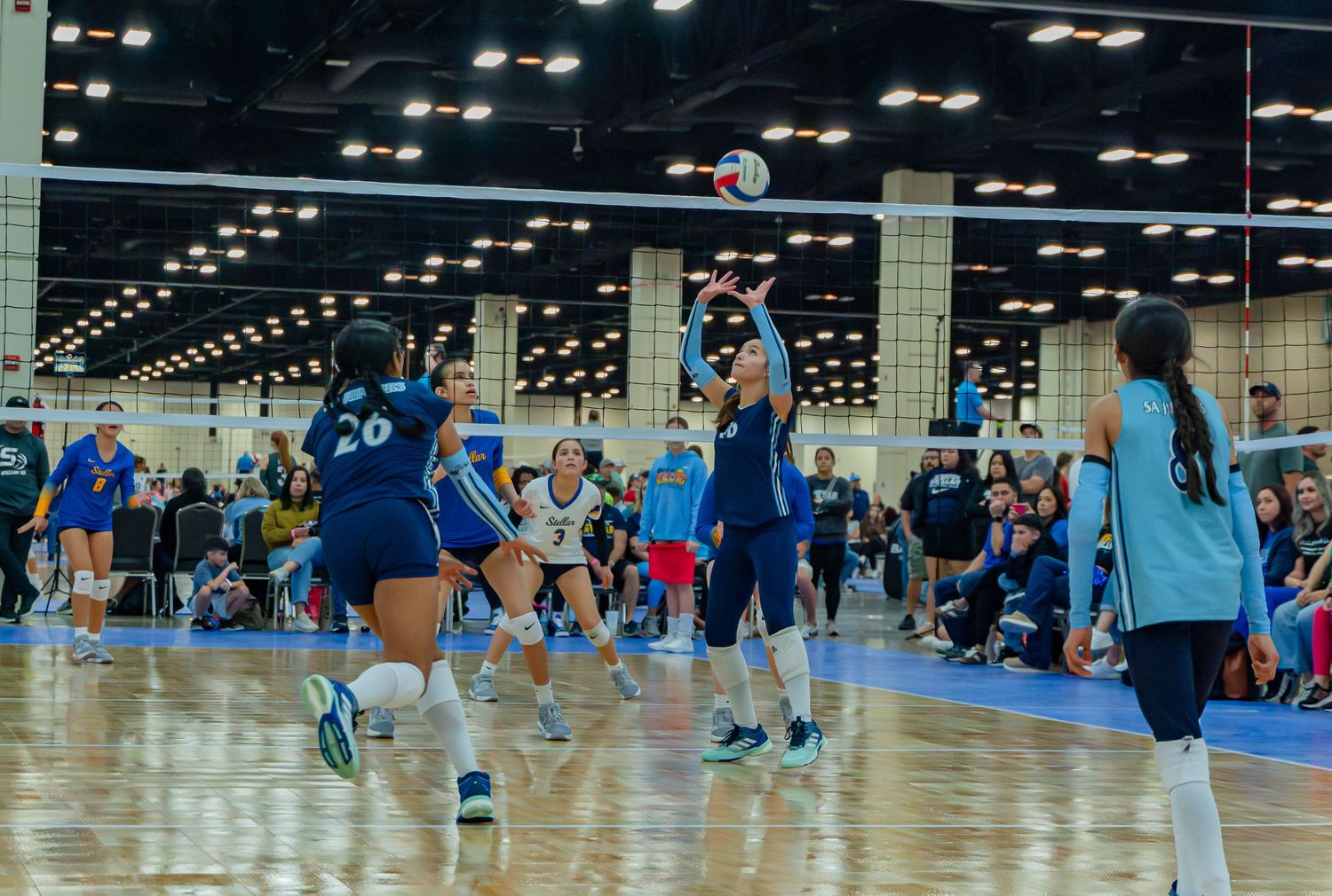 Wide view of indoor volleyball tournament with multiple courts and players in a large convention center space.