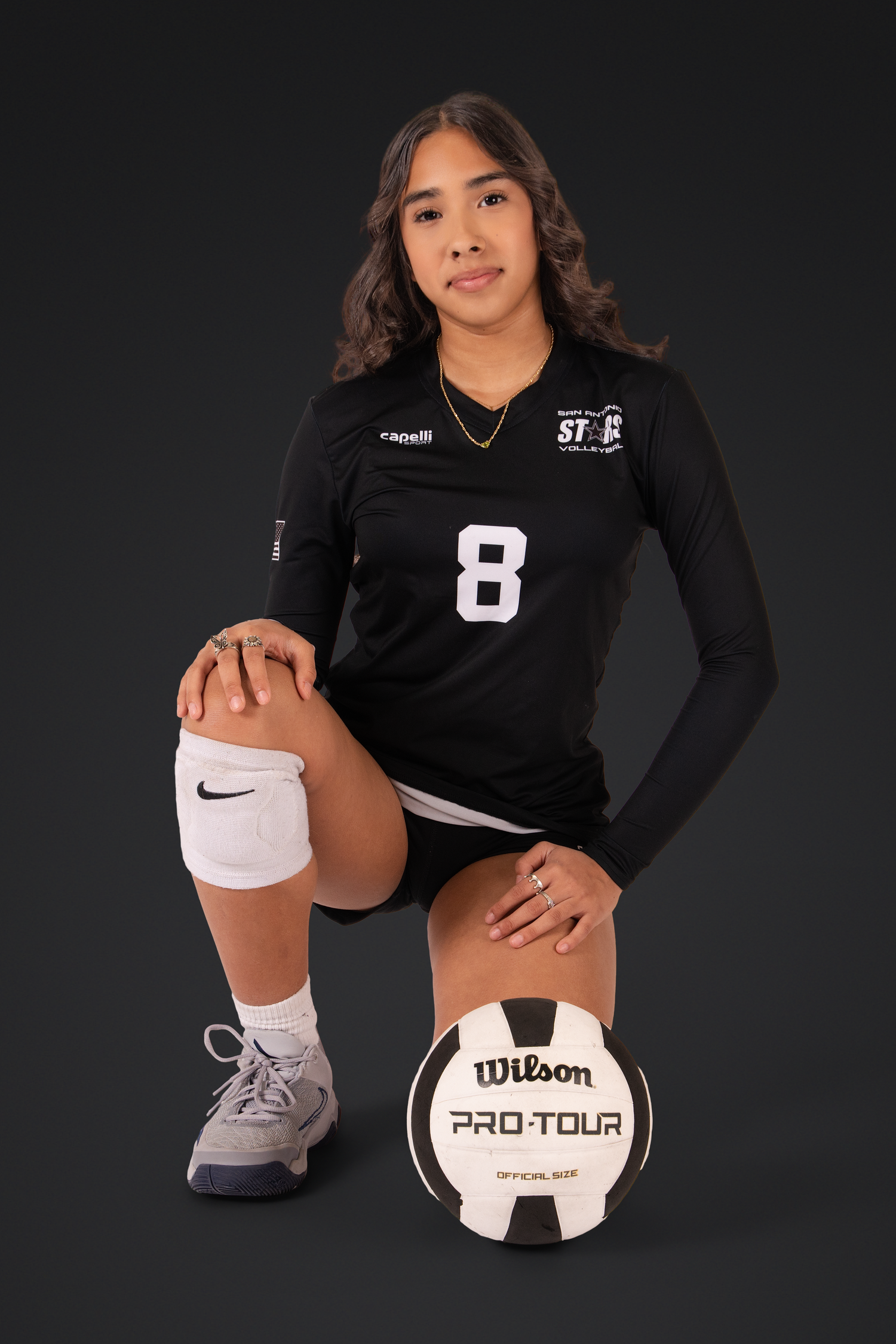 Athlete in black volleyball jersey poses with Wilson Pro Tour ball against dark backdrop.
