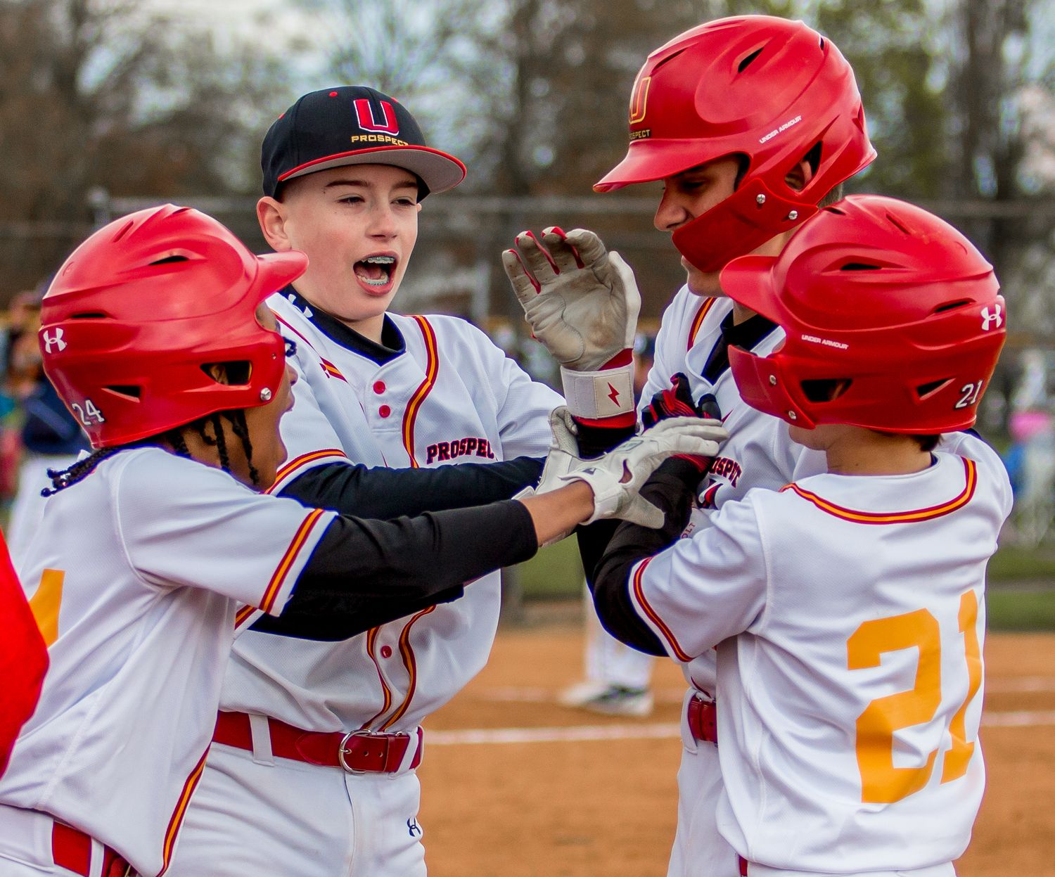 Youth baseball team celebrating in red helmets and white uniforms after scoring.