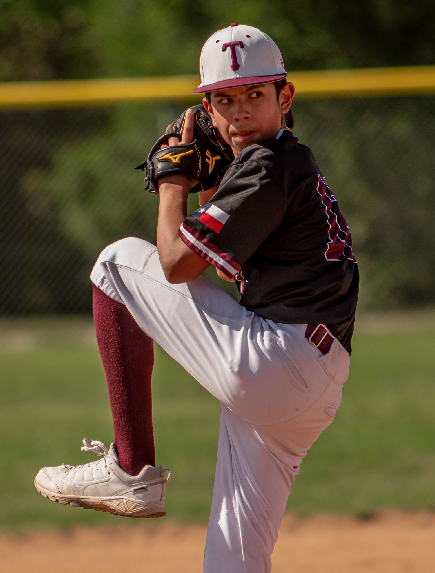 Baseball pitcher in black uniform and cap winds up for pitch delivery.
