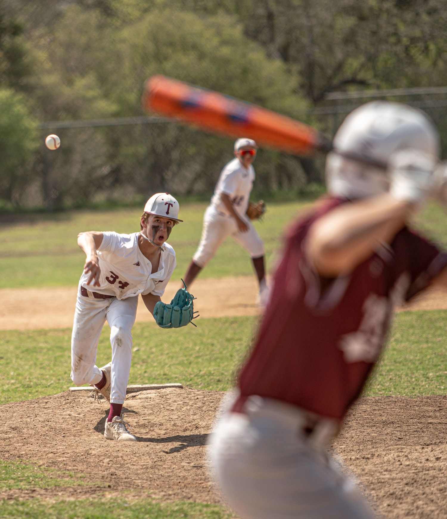 Baseball pitcher delivers pitch from mound while batter prepares to swing.