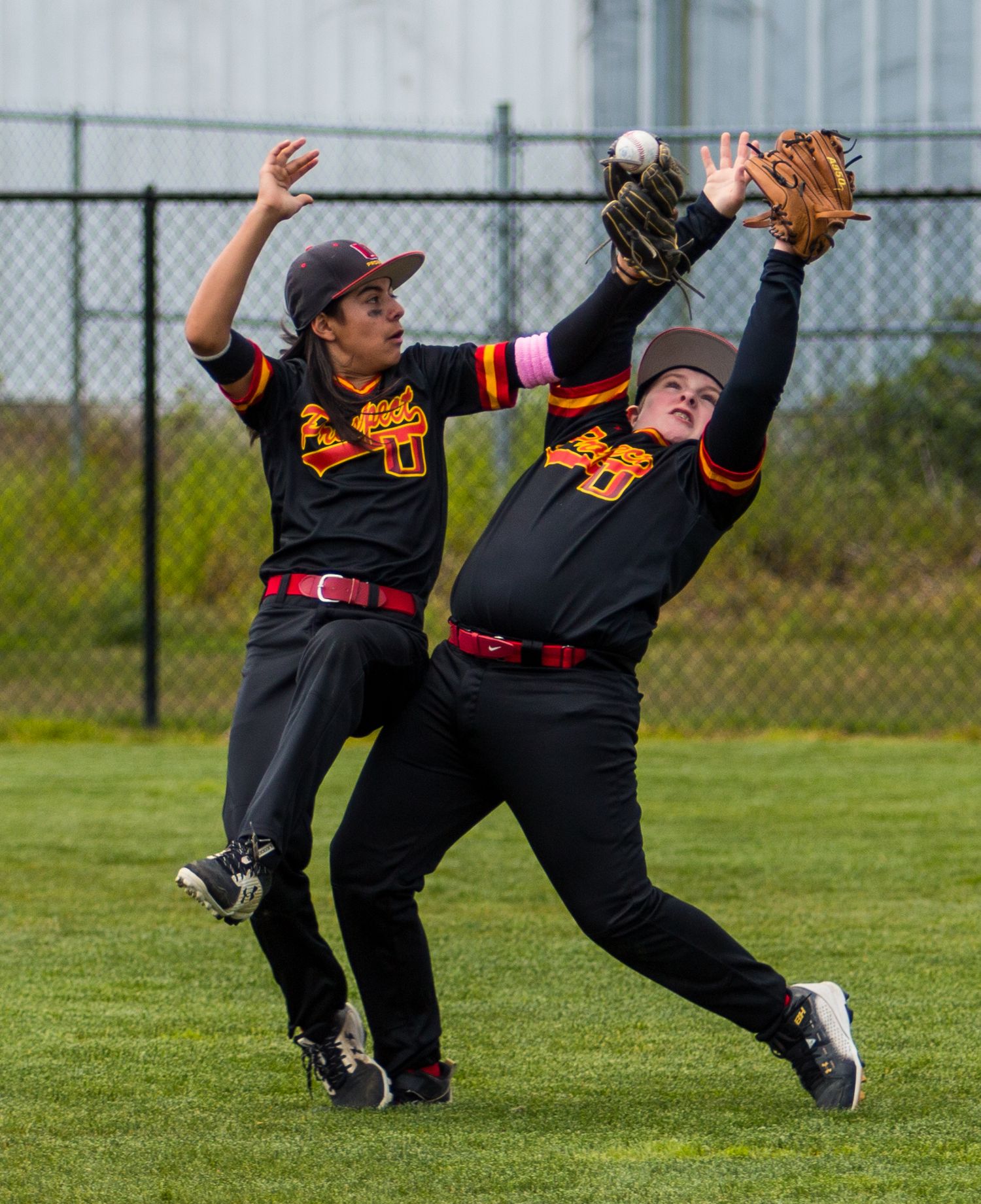 Two baseball players in black uniforms leap to catch a fly ball in the outfield.