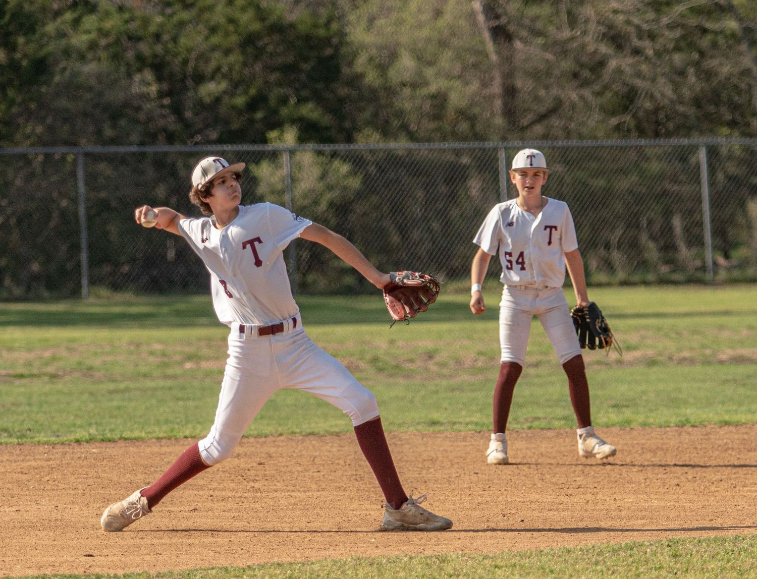 Baseball infielder throws ball during game while teammate stands ready in background.