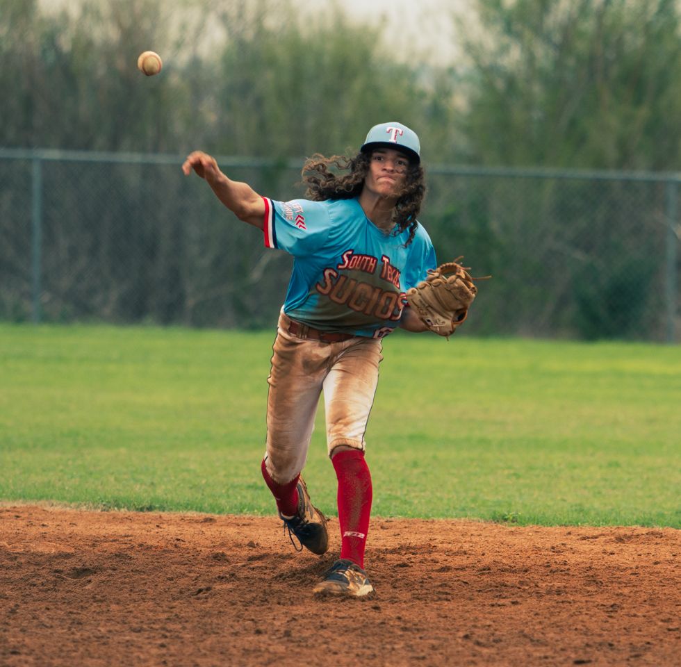 A youth baseball pitcher in mid-throw motion on a dirt mound wearing a light blue jersey and red socks.