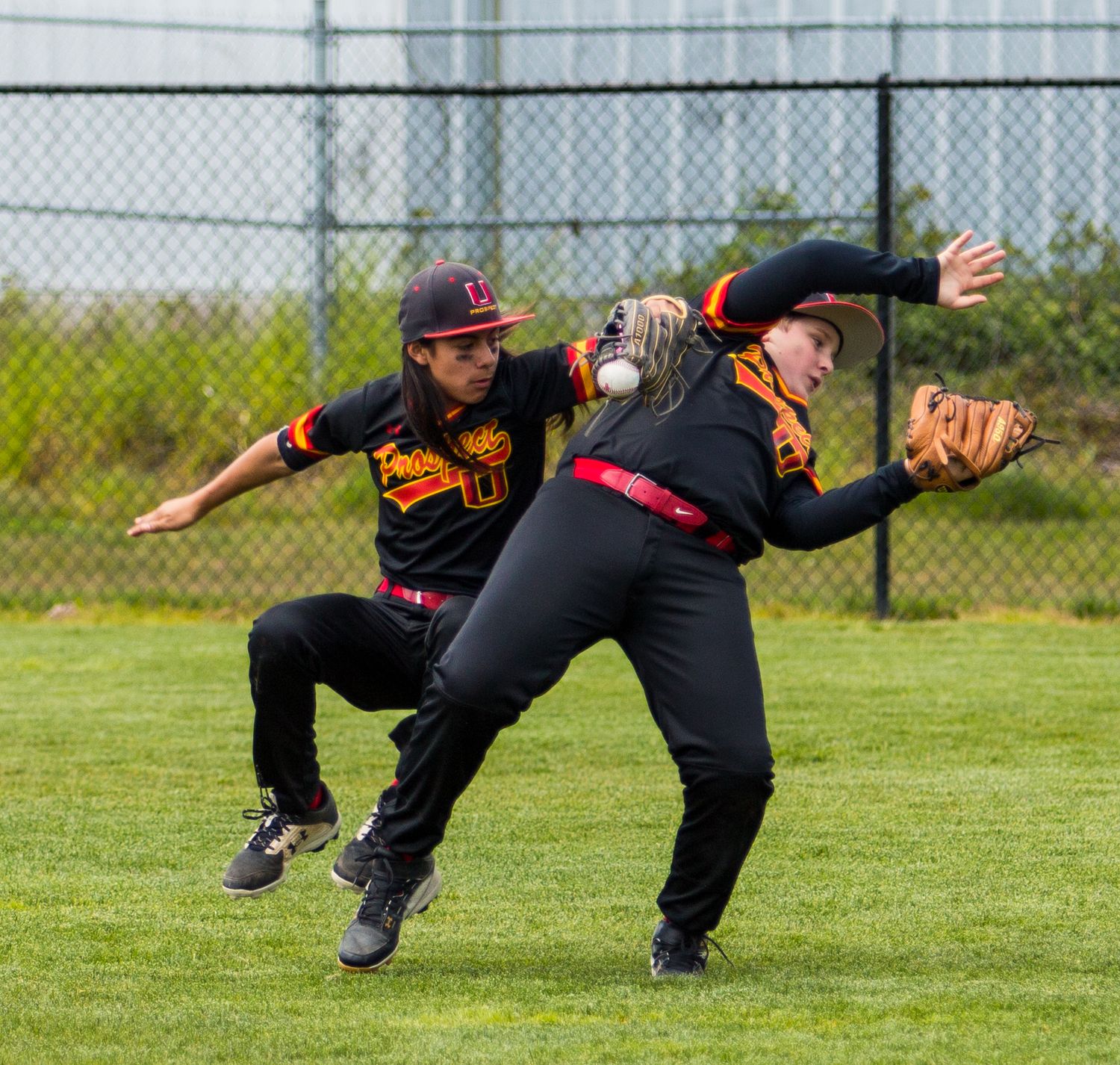 Baseball teammates in black uniforms attempt to catch a pop fly ball in the outfield.