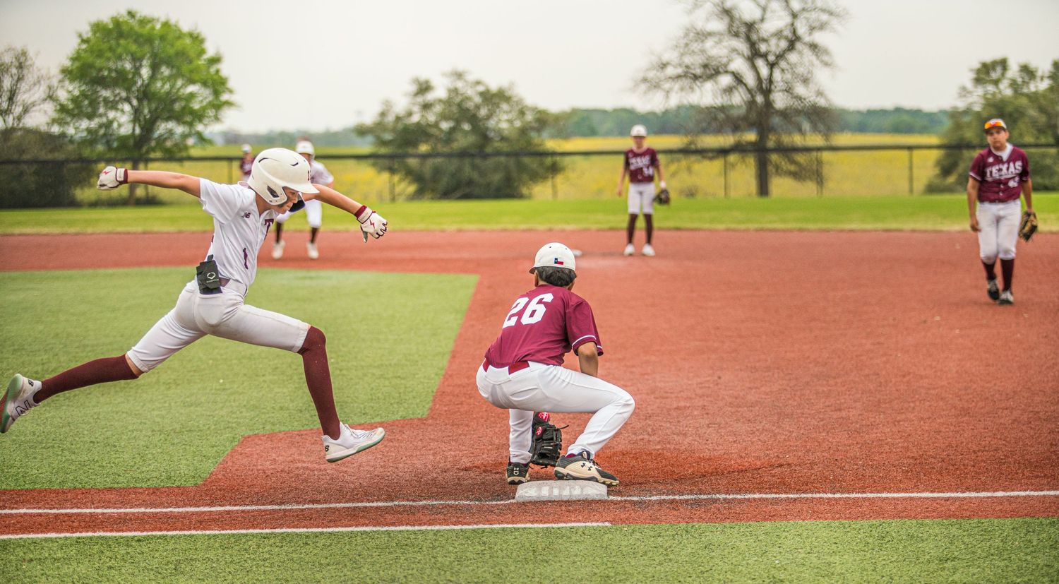 Runner sprints toward first base as fielder prepares to catch throw.