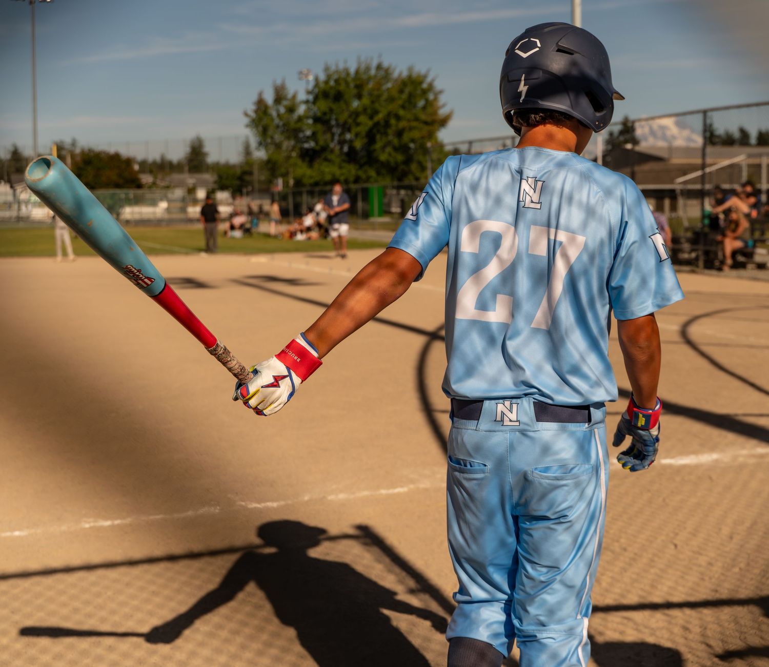 Baseball player in light blue uniform swings bat during game on sunny outdoor field.