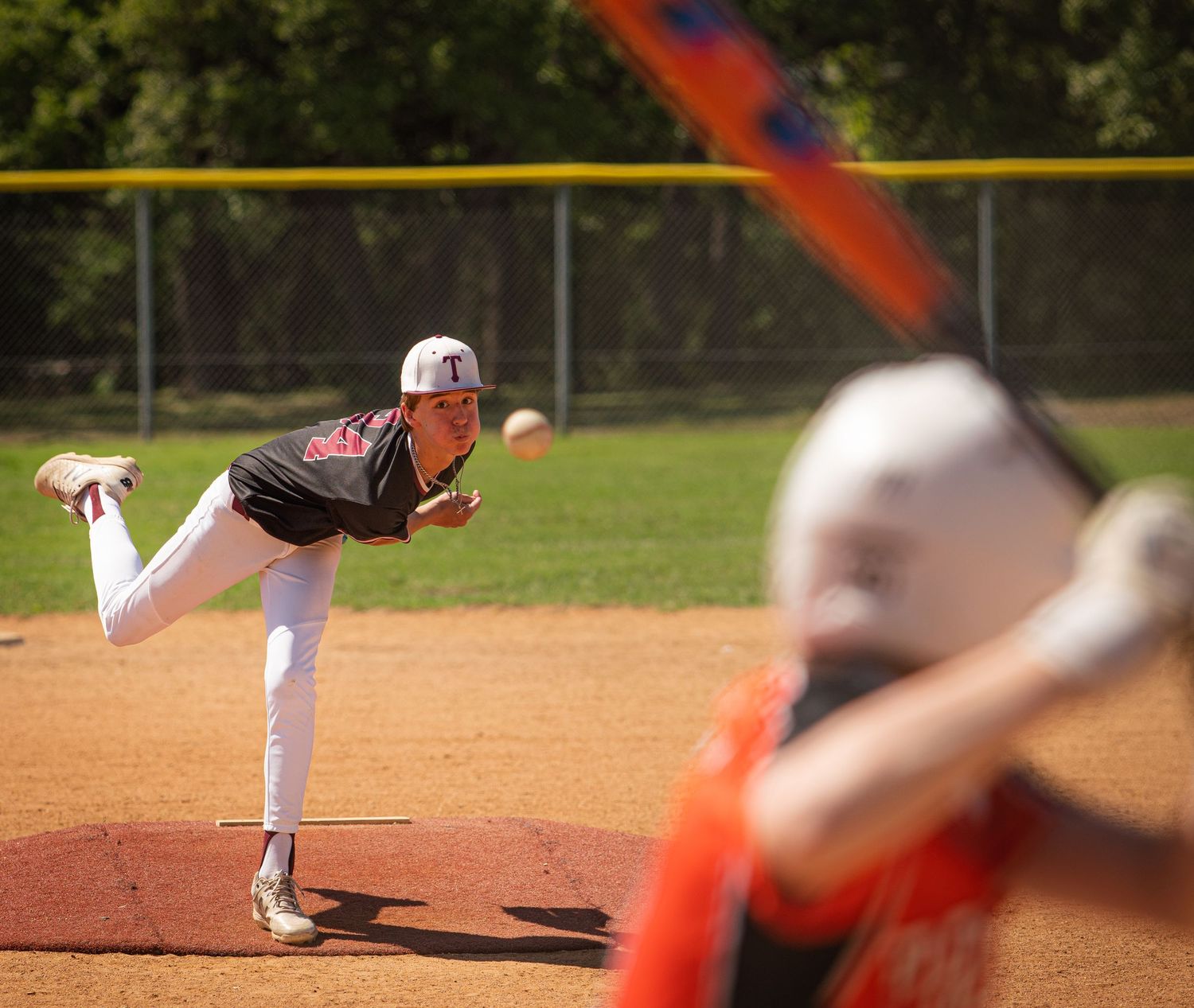 Baseball pitcher follows through on delivery as batter awaits pitch in background.