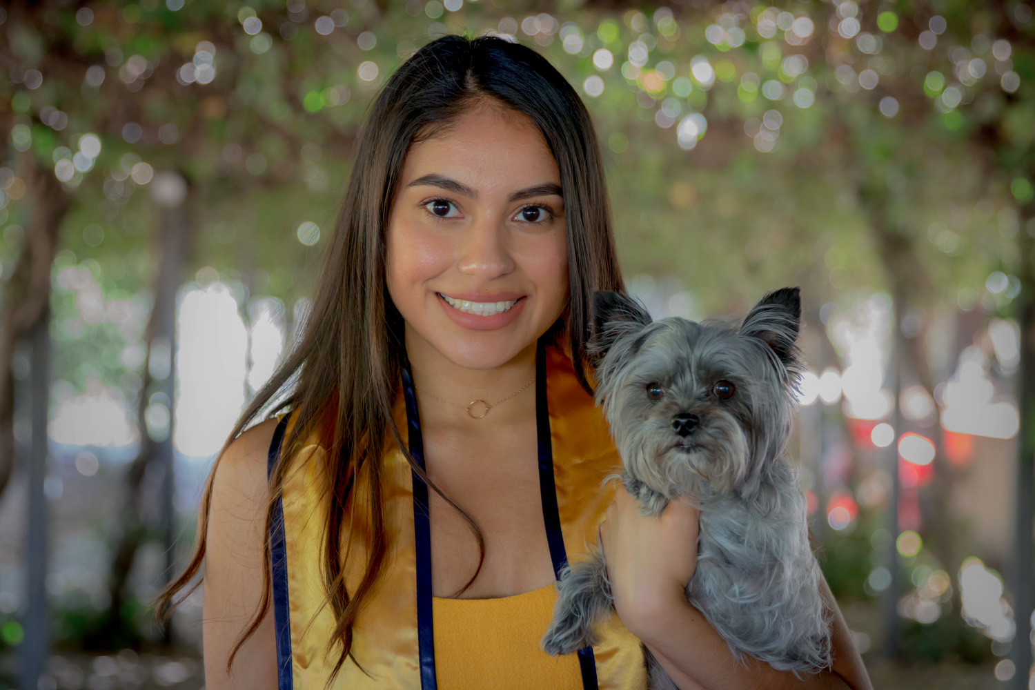 Graduate with small grey dog poses outdoors during graduation photoshoot.