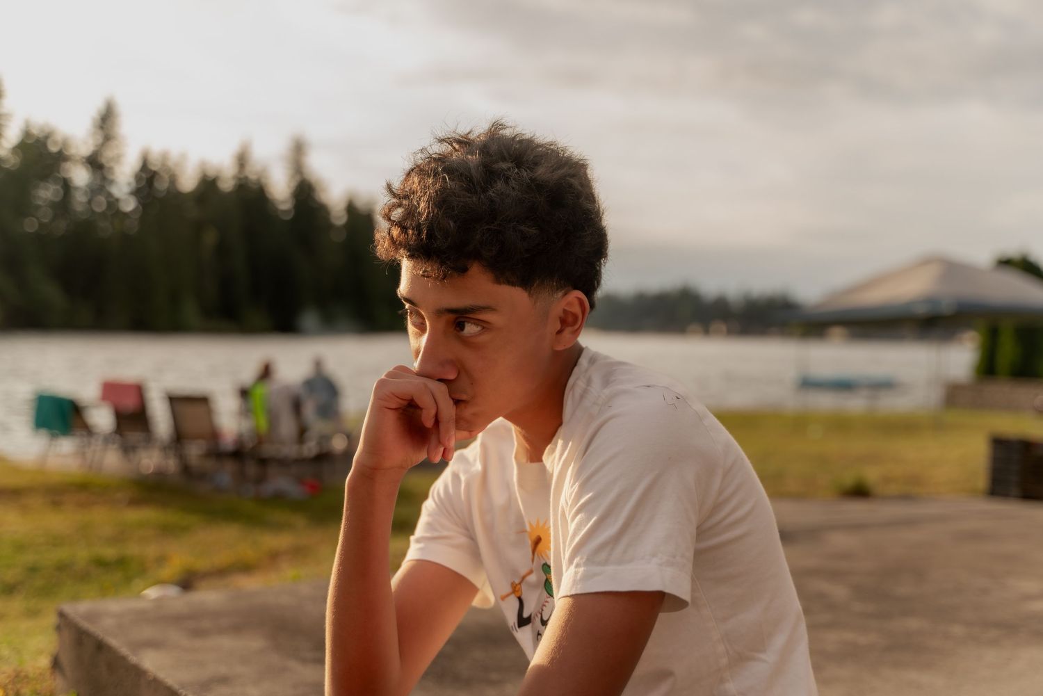 Person in white shirt sitting outdoors during golden hour with trees in background.