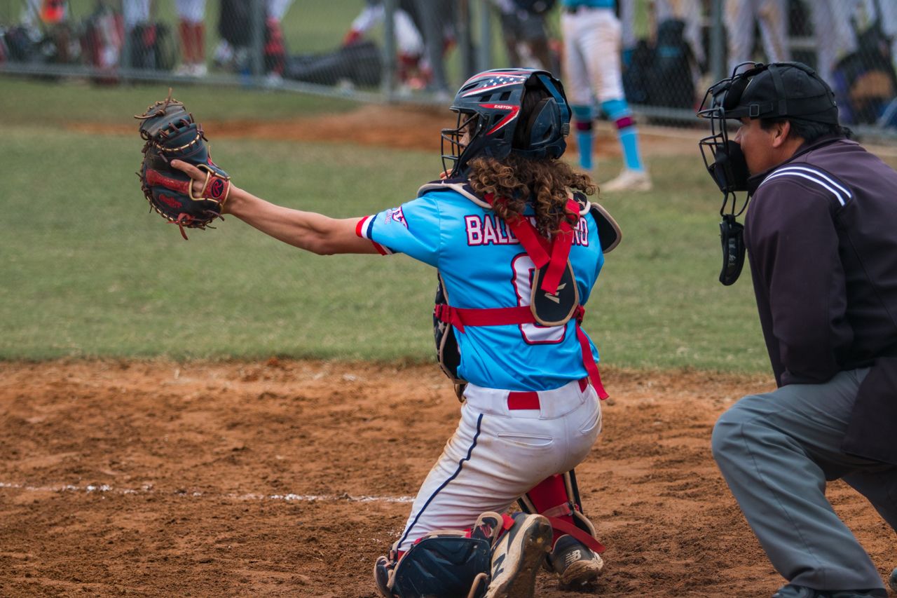 Baseball catcher in bright blue jersey crouches behind home plate ready to receive a pitch during a game.