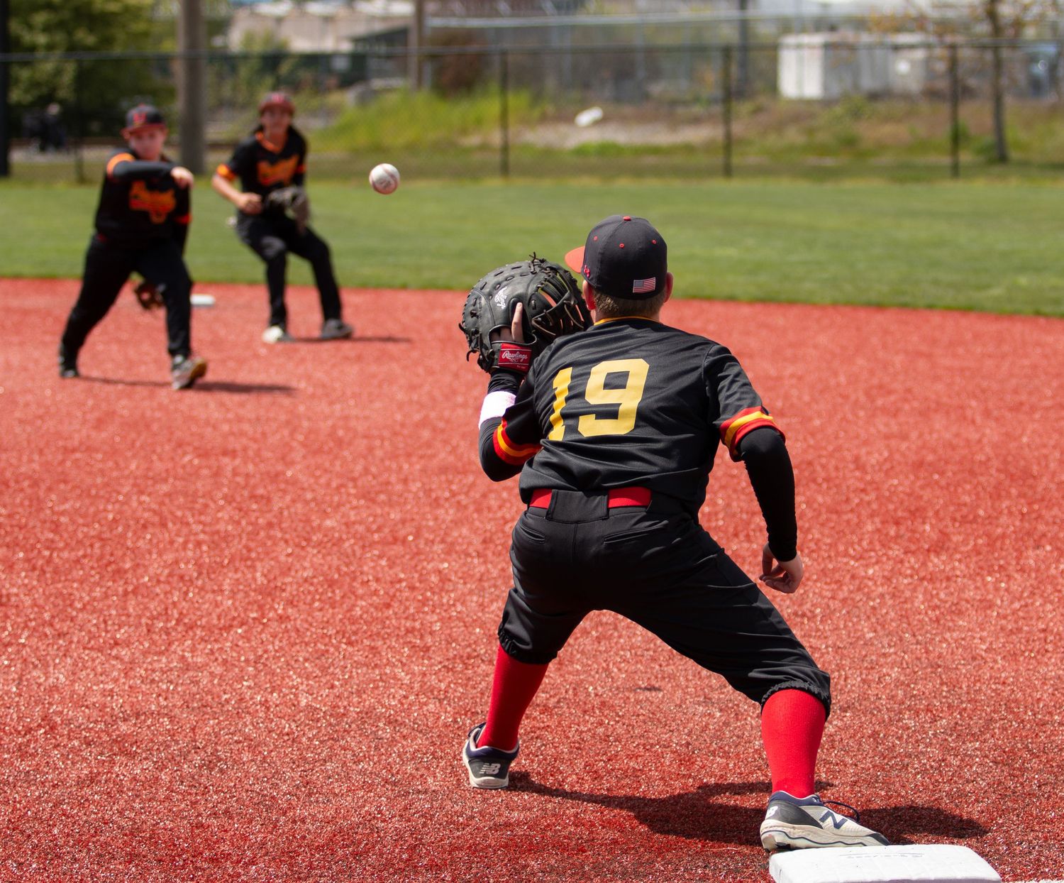 Baseball infielders in black uniforms prepare for play on red turf field.