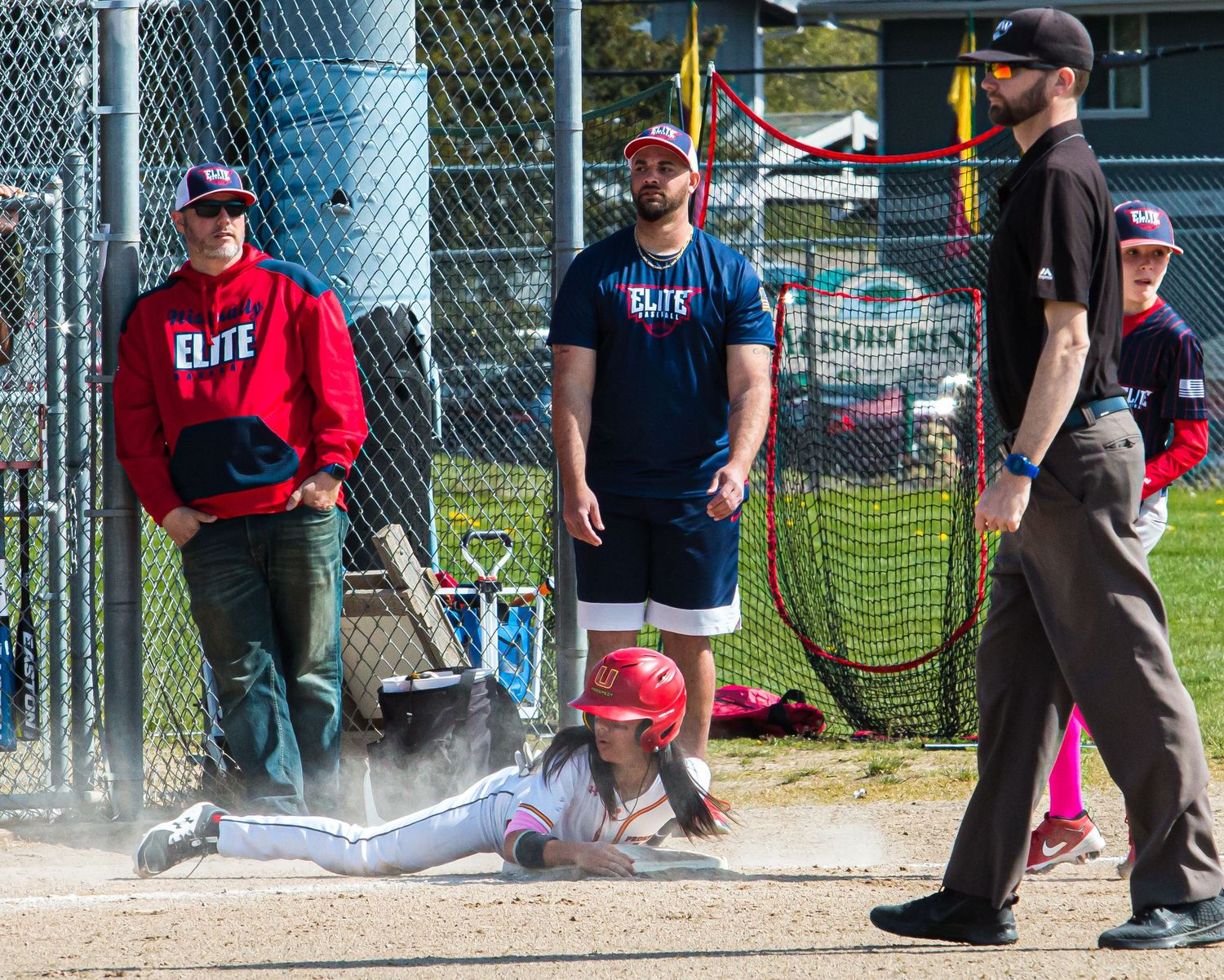 Baseball players and spectators gather near the dugout fence during a game.