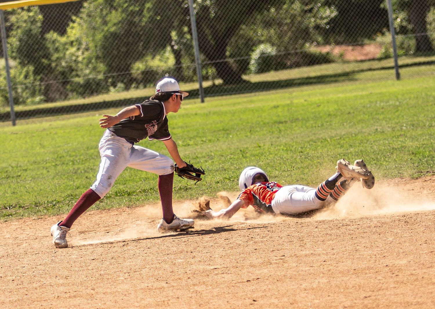Baseball players compete for the ball during a sliding play at the base.