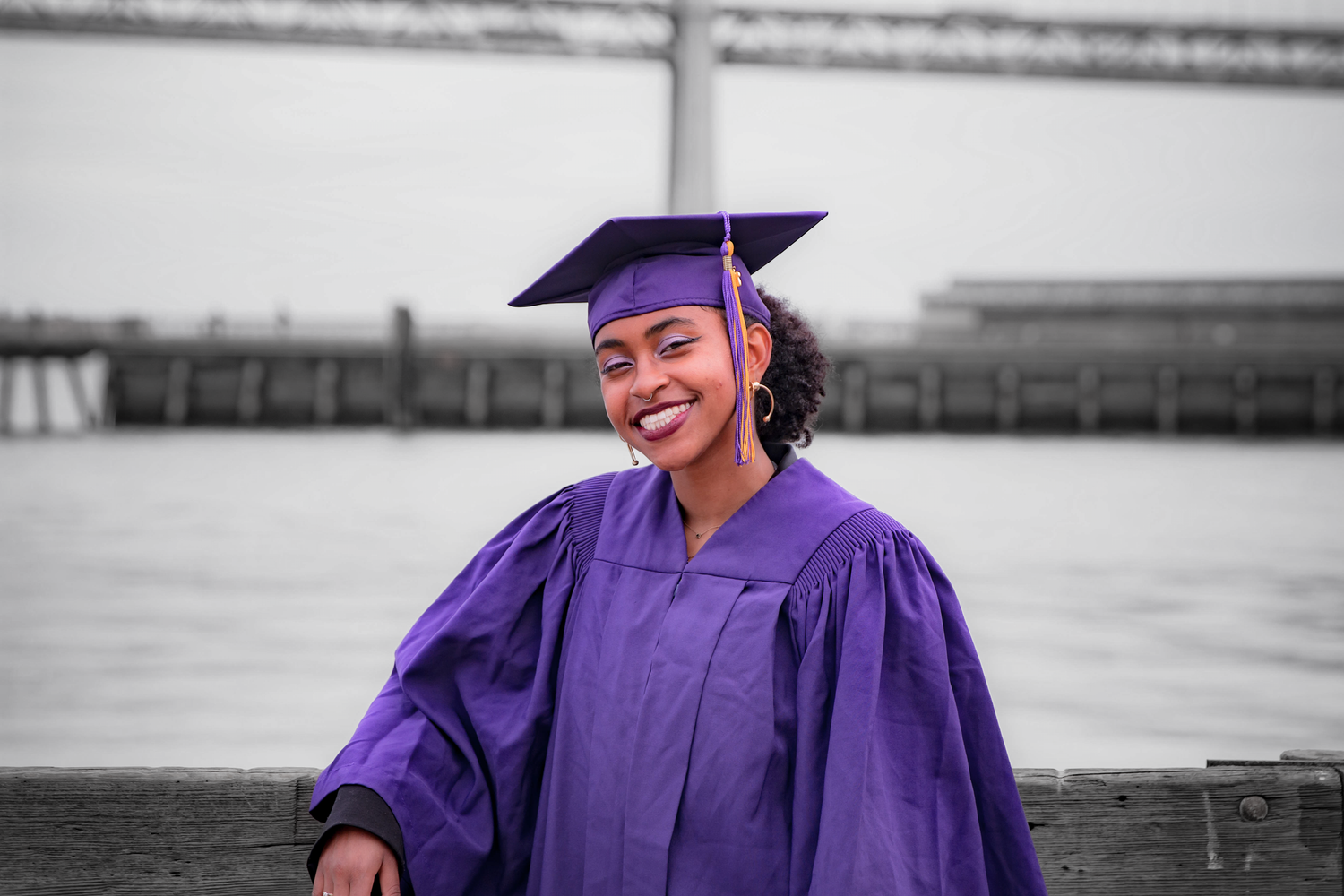Graduate in purple cap and gown smiling during outdoor commencement ceremony.
