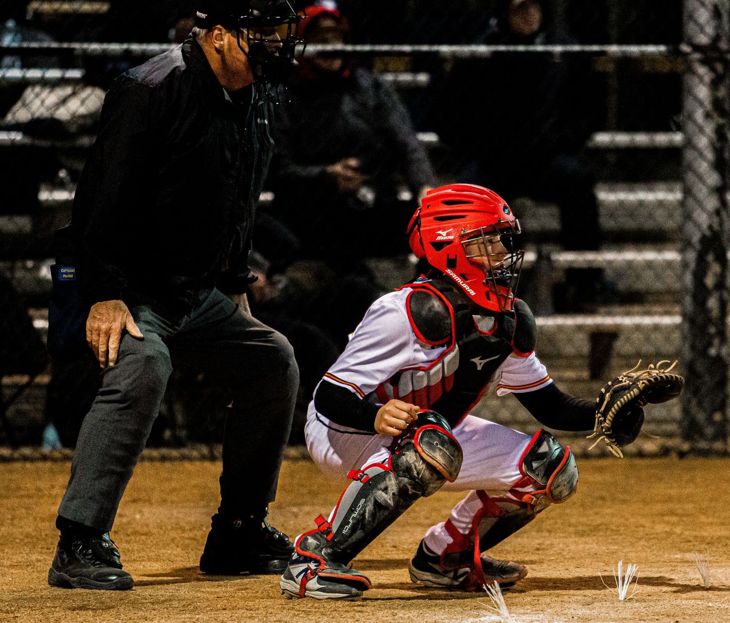 Night baseball game showing catcher in position behind home plate.