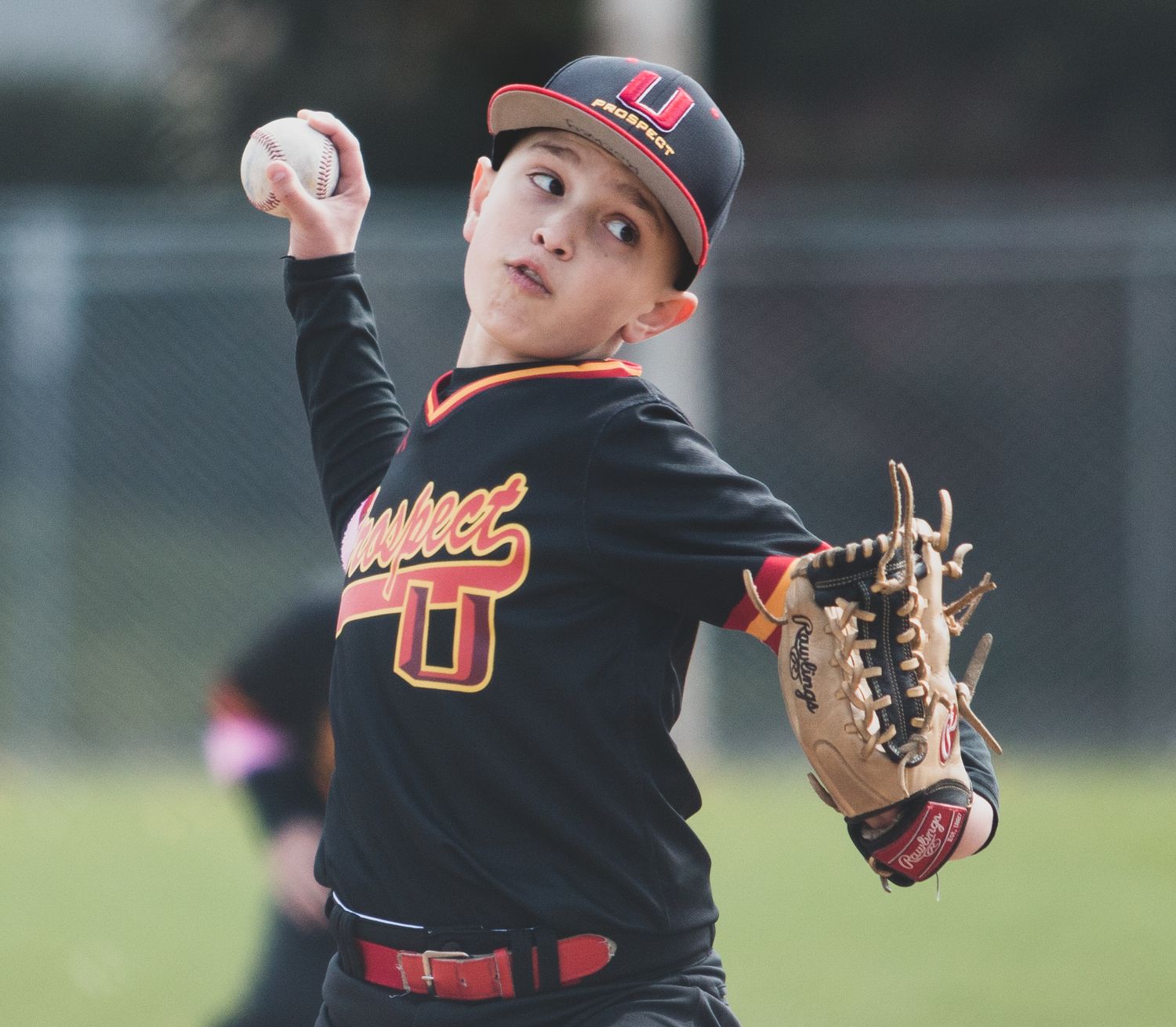 Baseball pitcher in black uniform winding up to throw during a game.