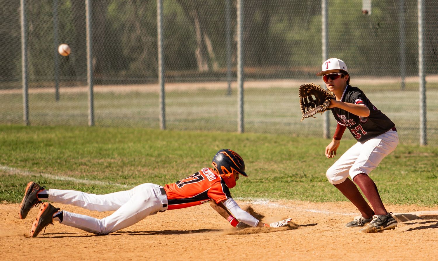 Baseball player slides into base while defender attempts to make the tag.