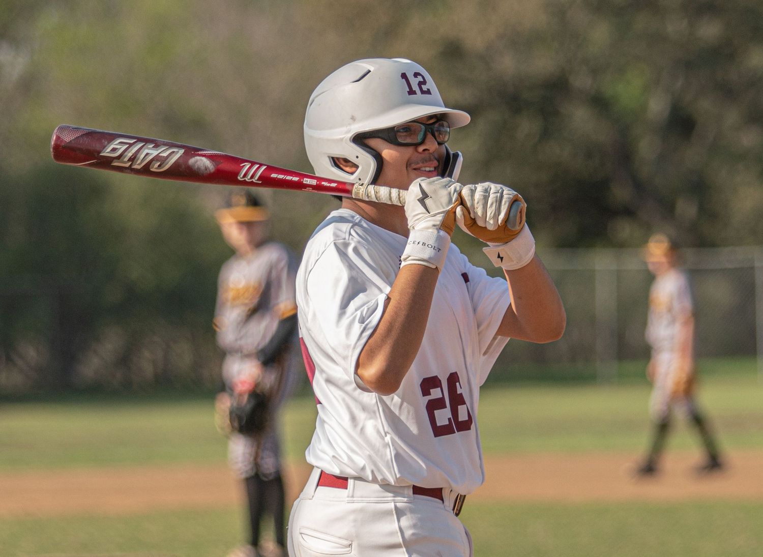 Baseball players in white uniforms at bat during daytime game on grass field.