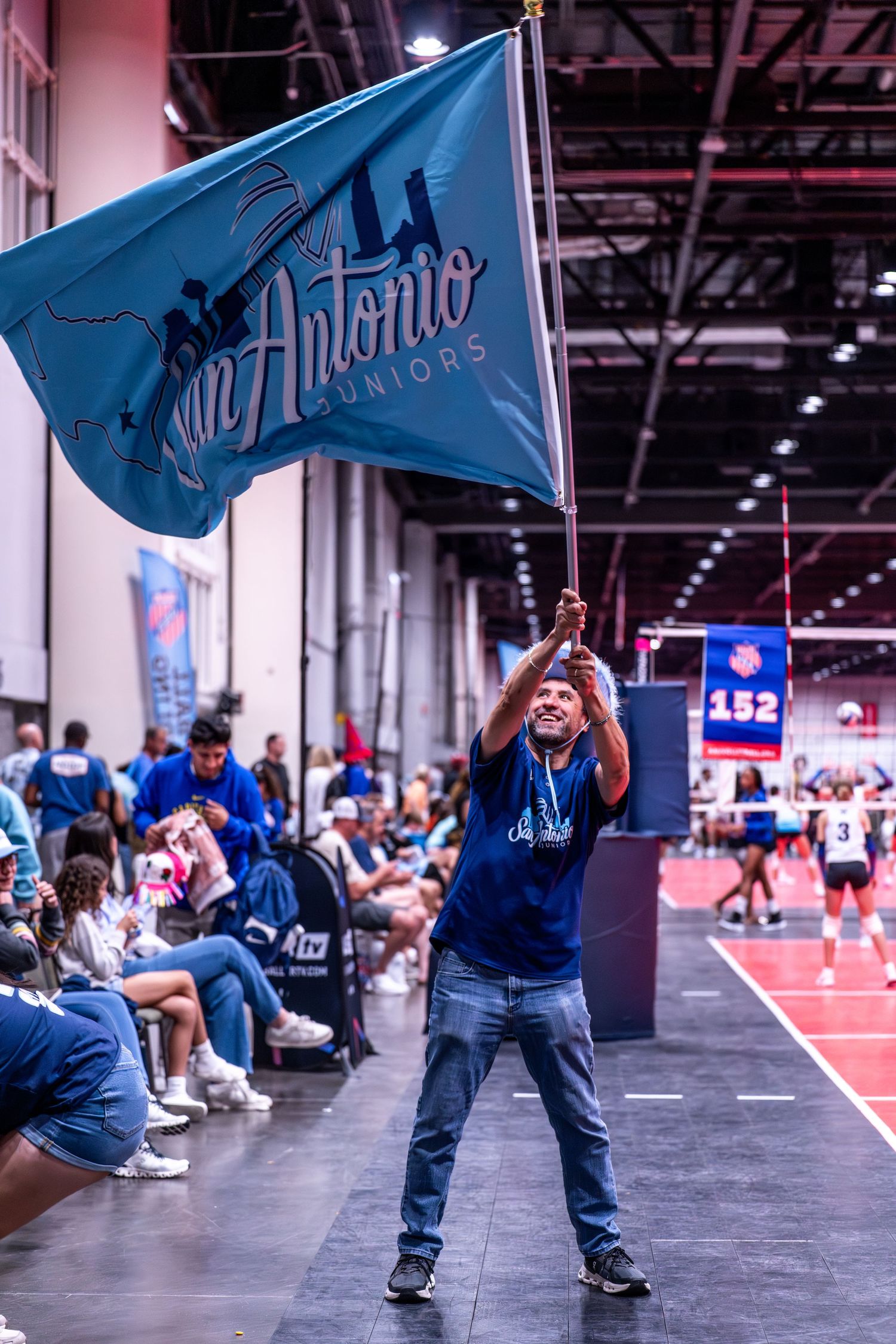 Fan waves team flag enthusiastically during volleyball tournament.