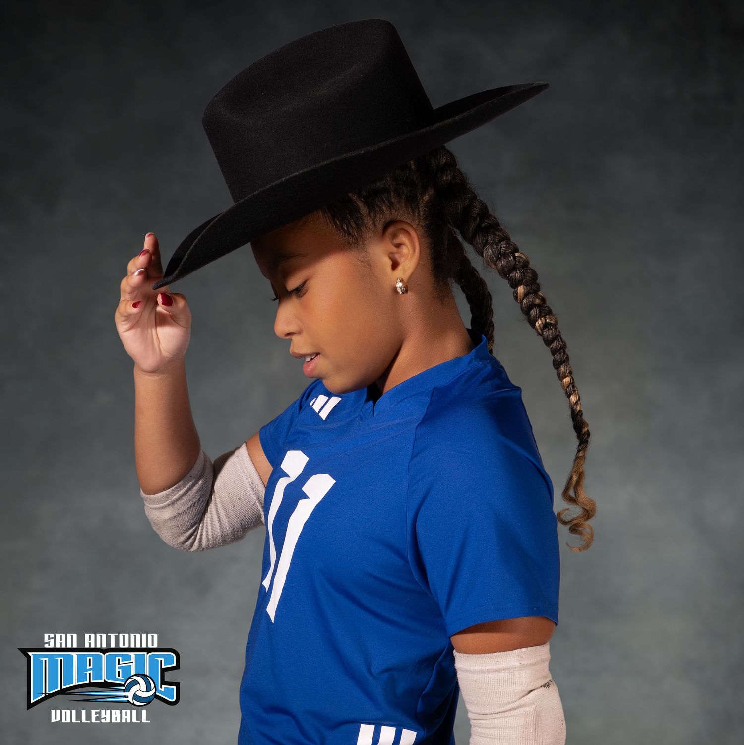 Volleyball player in blue jersey with cowboy hat poses against dark background.