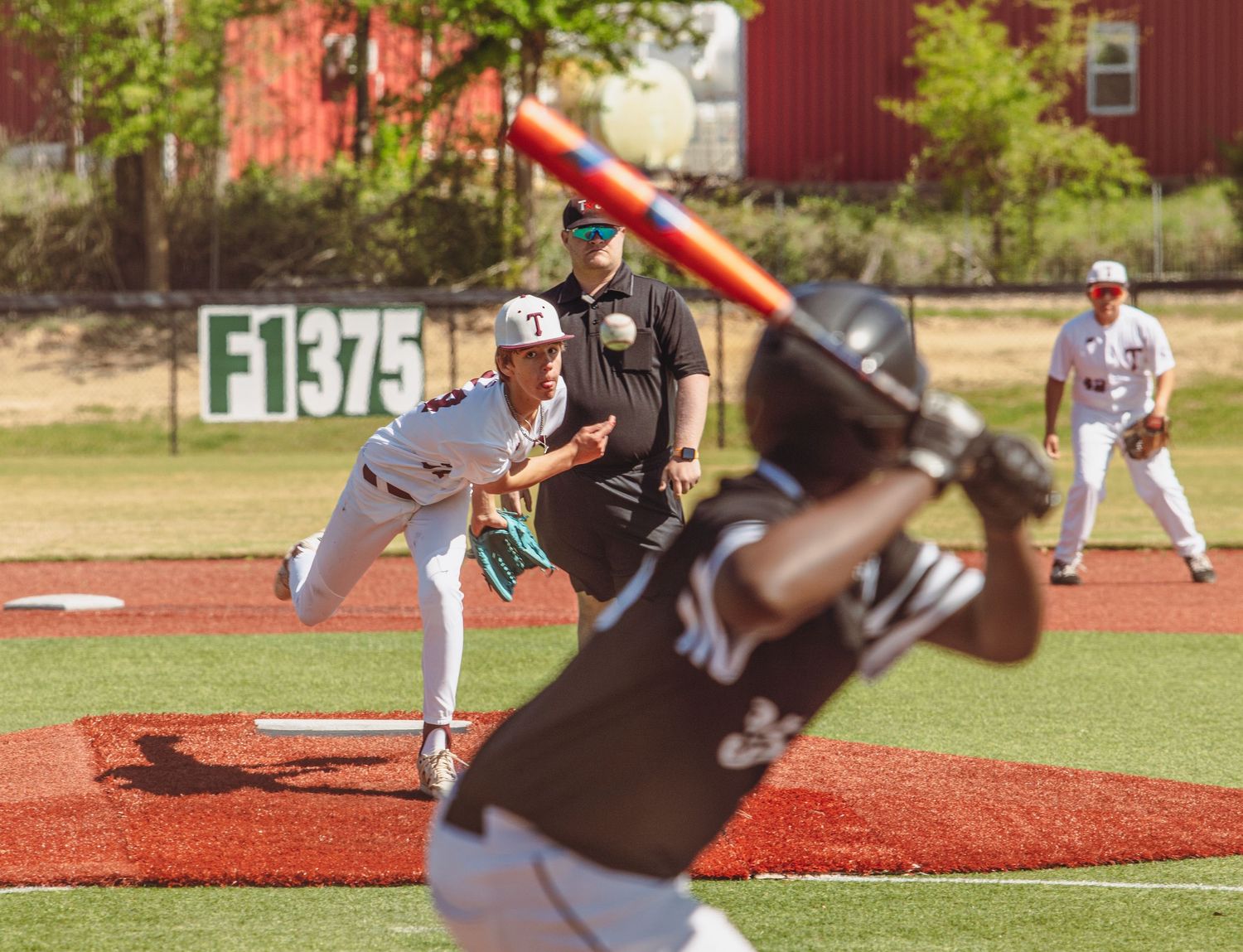 Baseball game action showing pitcher delivering pitch while batter prepares to swing.