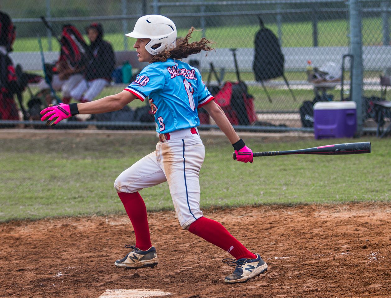 A baseball player in a light blue jersey and red pants stands on the pitcher's mound during a game.