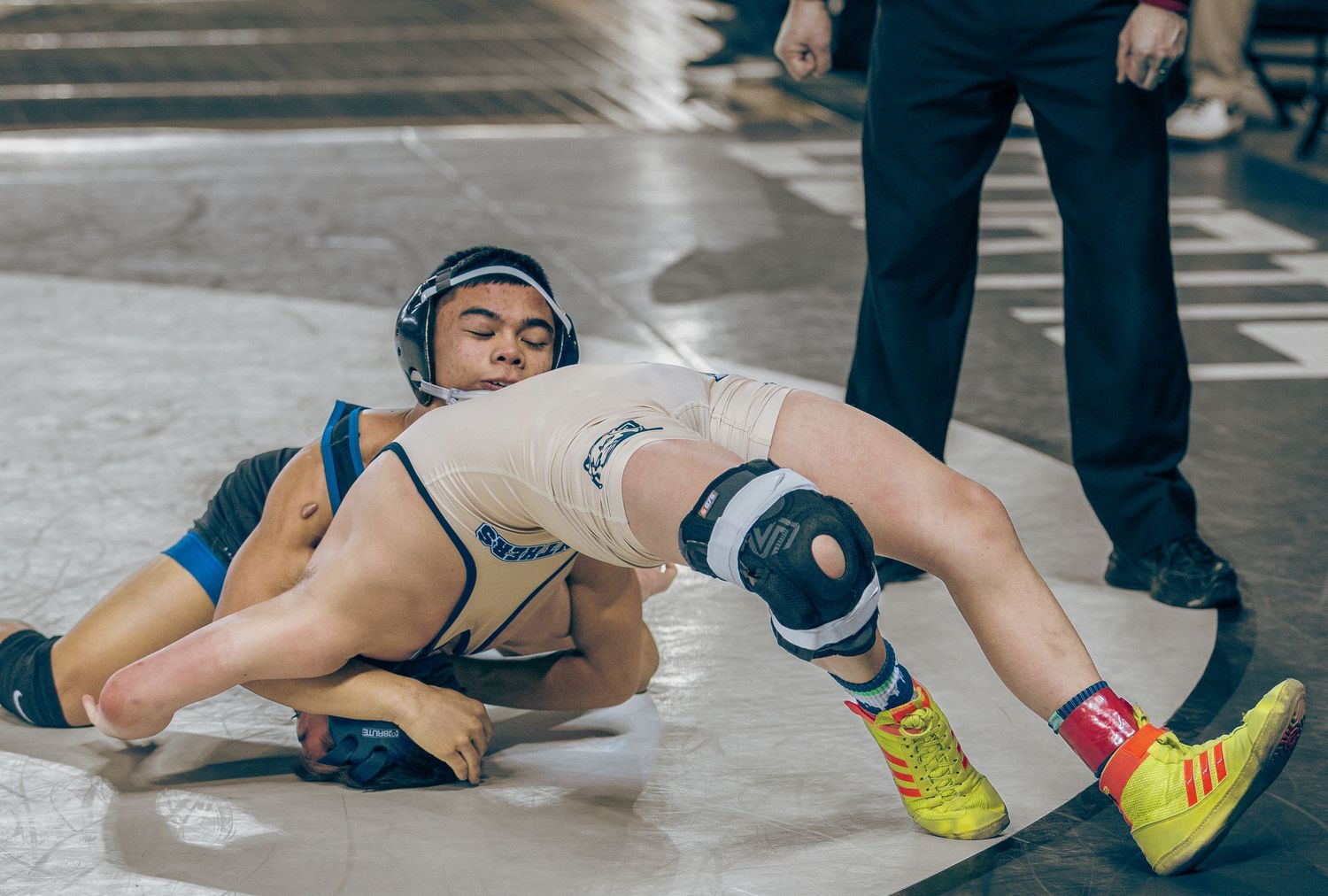 Wrestlers grapple on the mat during an intense competition match.