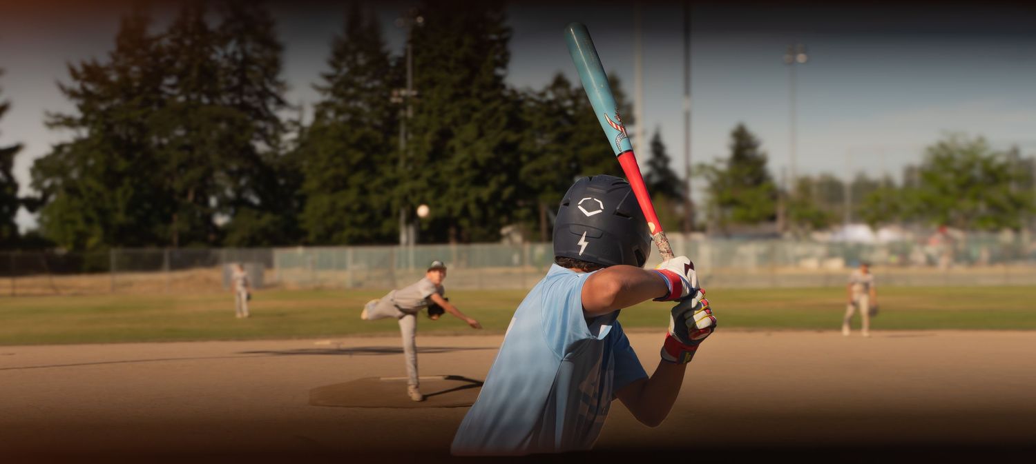 Baseball players on field during sunset game with stadium lights visible.