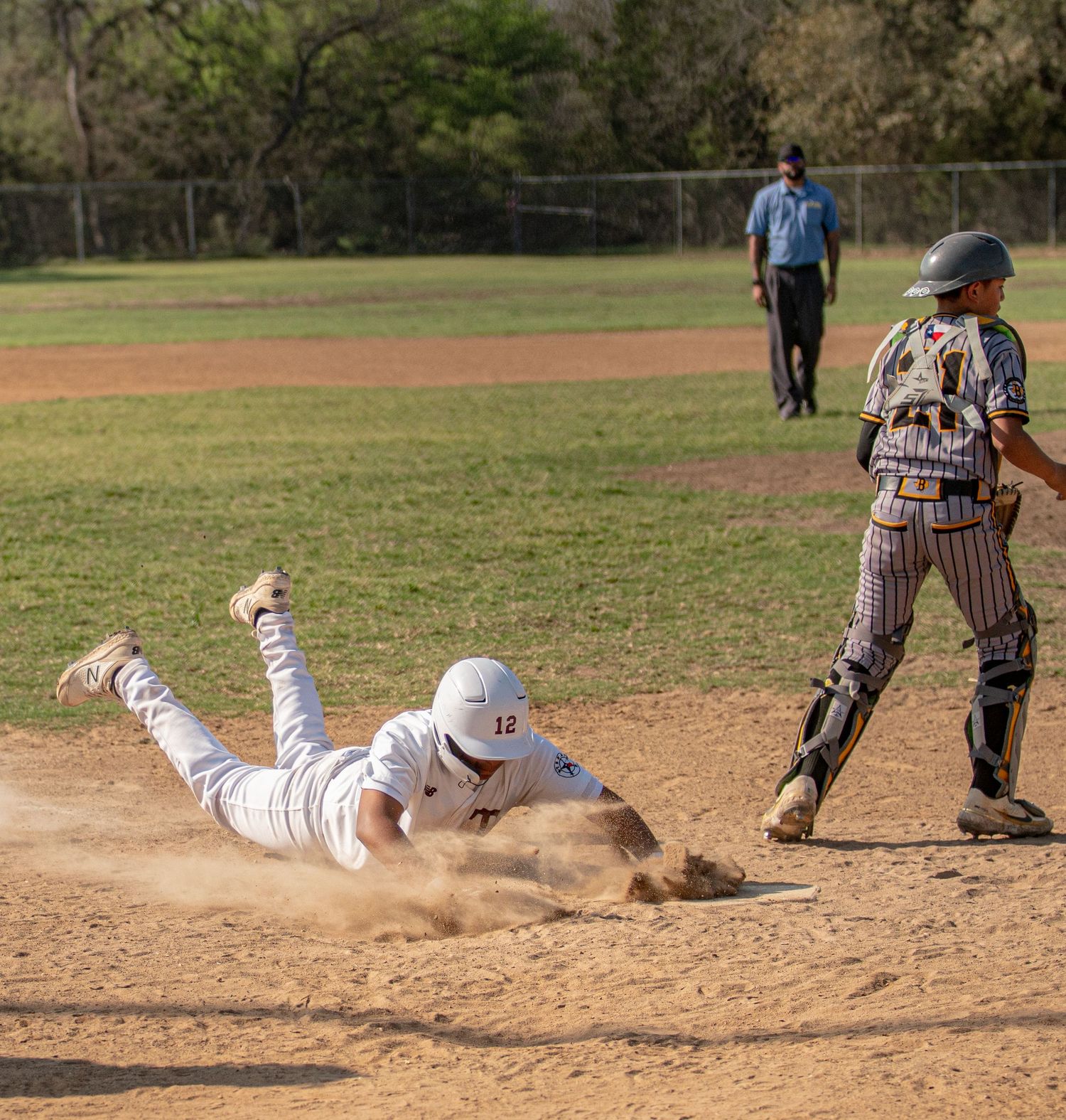 Baseball player slides head-first into base creating dust cloud during game play.