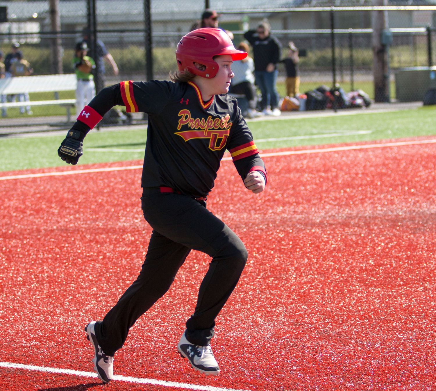Players in black uniforms practice sliding techniques on red artificial turf.