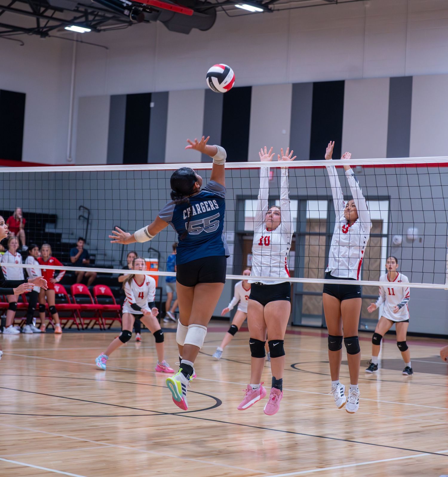 Volleyball players from opposing teams competing at the net during an indoor match.