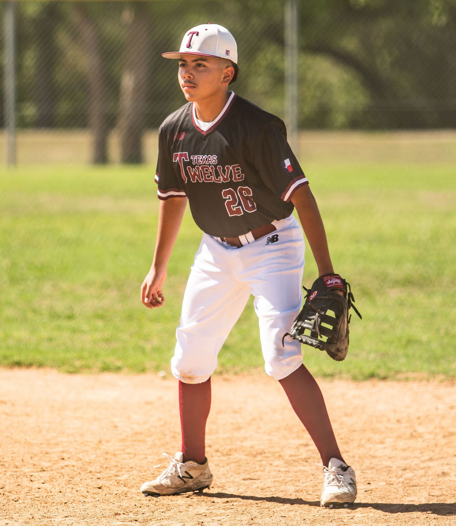Youth baseball player in uniform stands ready in fielding position on dirt infield.