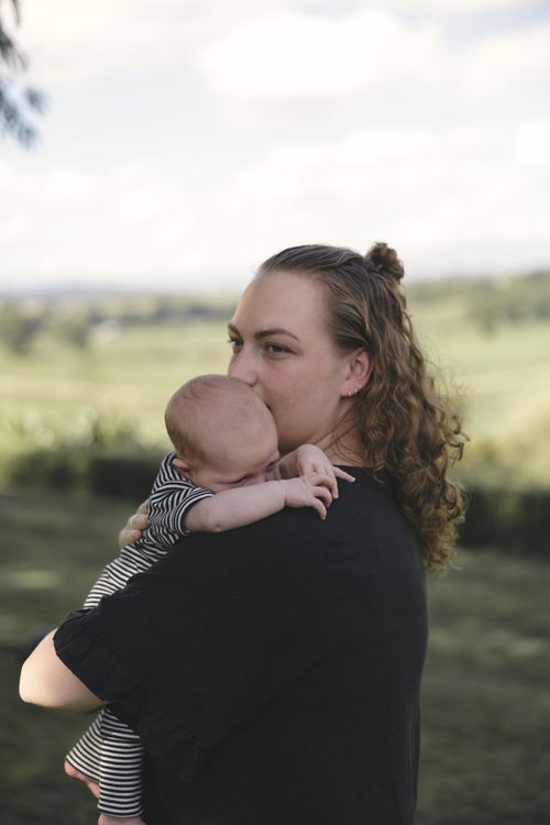 Mother gently holding her baby during a newborn photography session in the Bay of Plenty