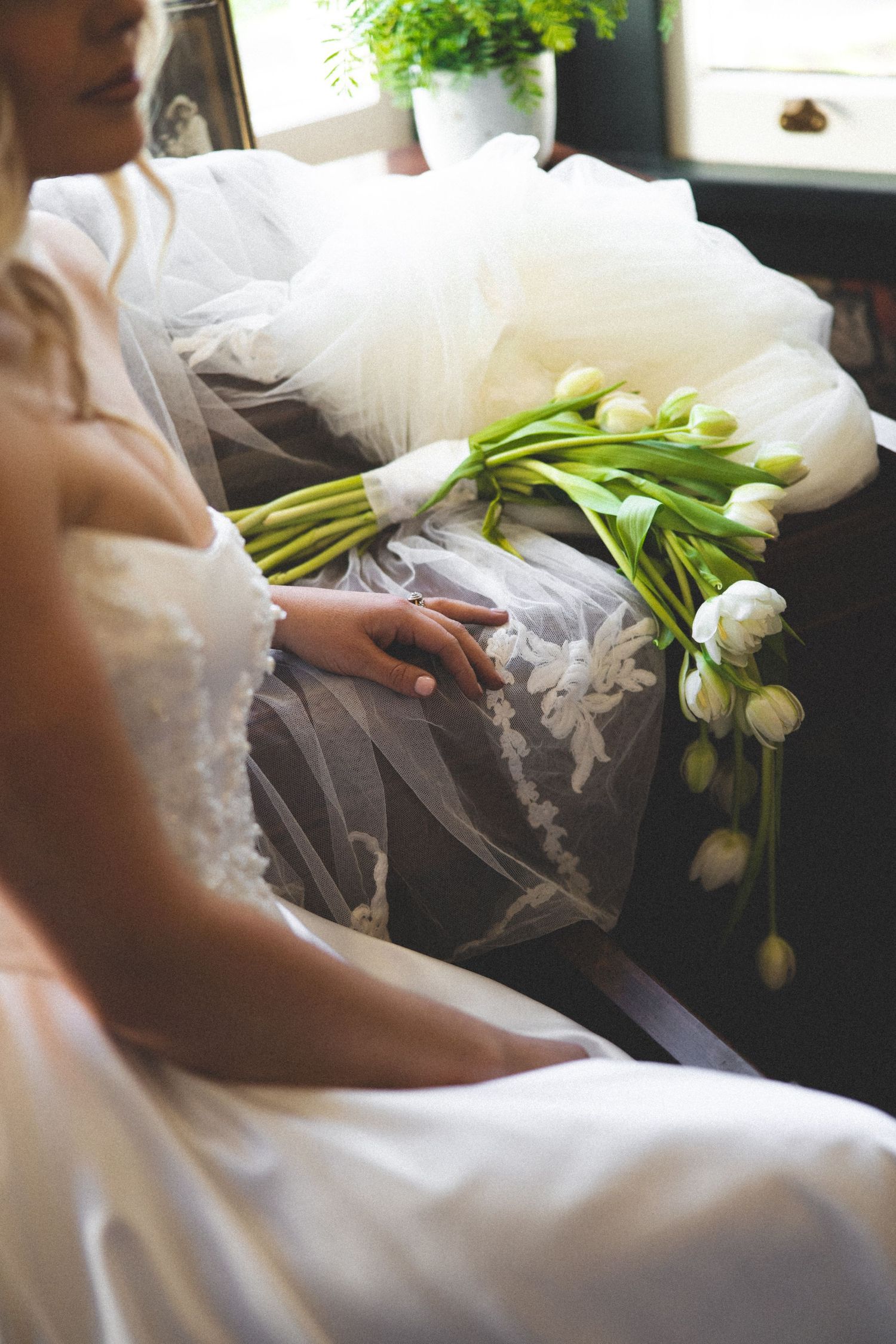 Bride in a white gown holding a white tulip bouquet next to her wedding dress and veil during getting-ready preparations for a Tauranga wedd