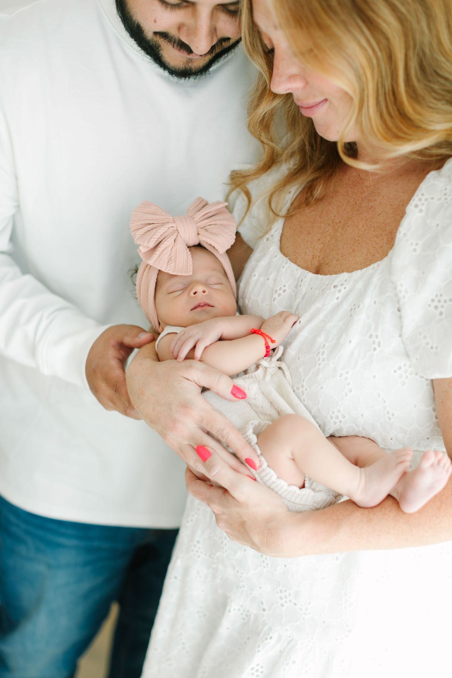 Parents in white and denim hold their newborn baby wearing pink in a series of tender indoor portrait shots.