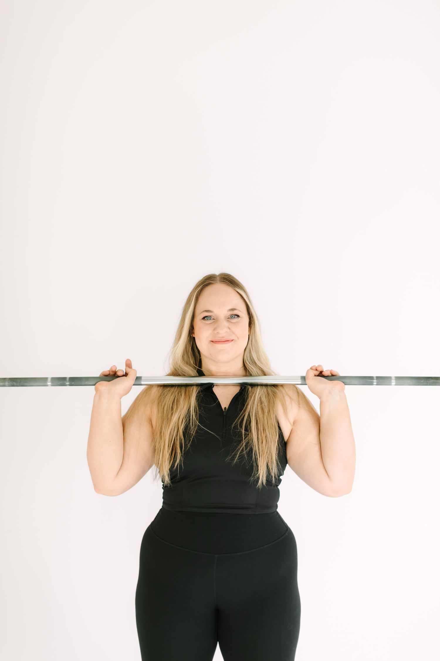 A person in black athletic wear demonstrates proper barbell positioning during an overhead press exercise.