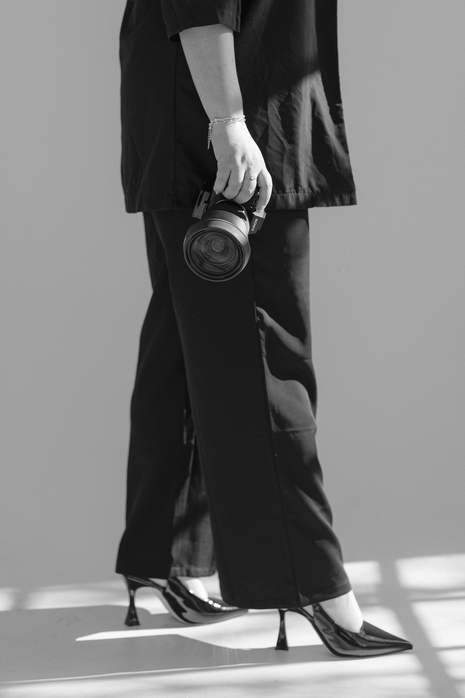 Black and white photo of legs wearing formal shoes and pants walking across a sunlit floor.