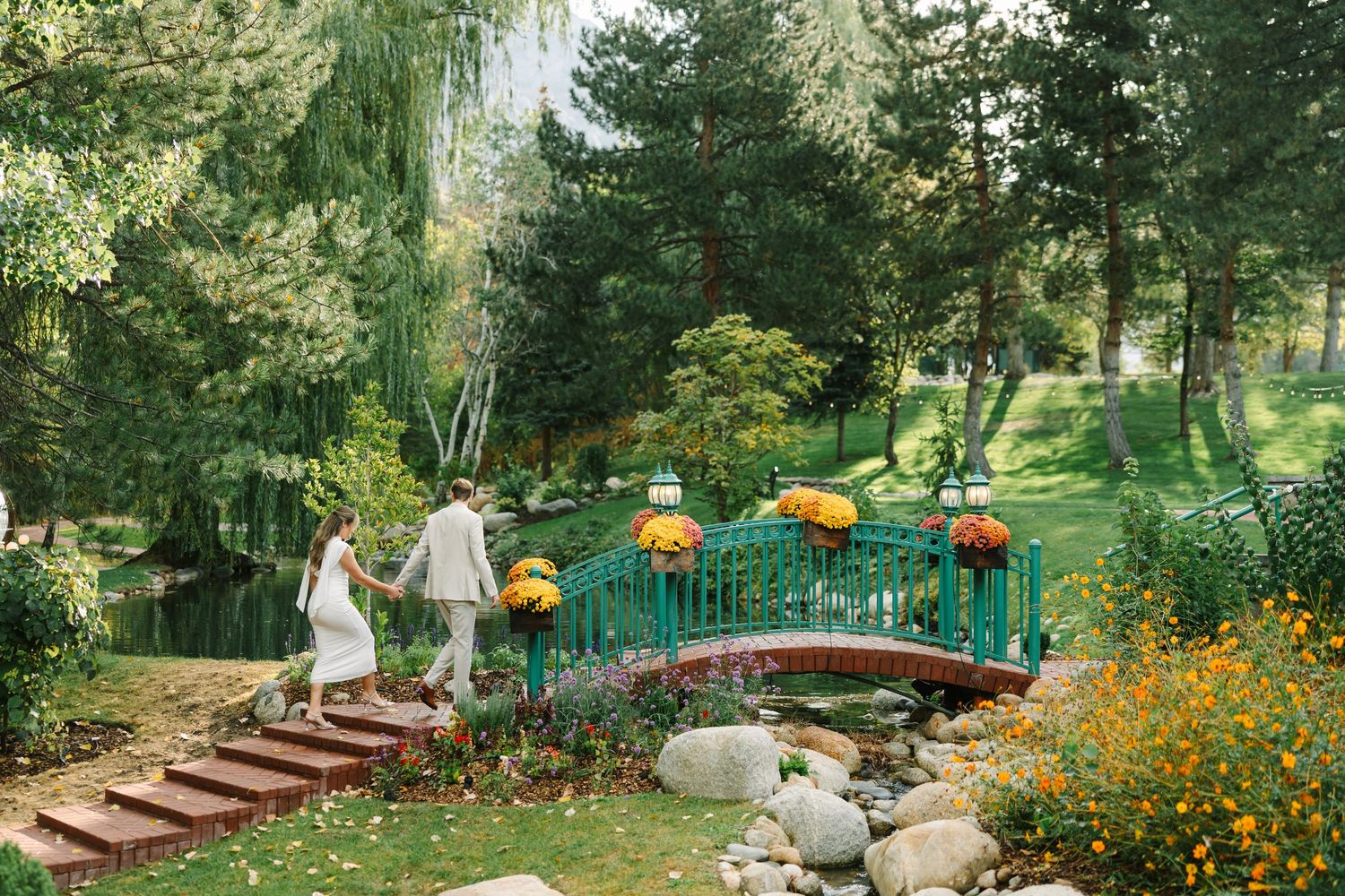 A scenic garden pathway features a red arched bridge, stone steps, and vibrant orange marigold flowers in bloom.
