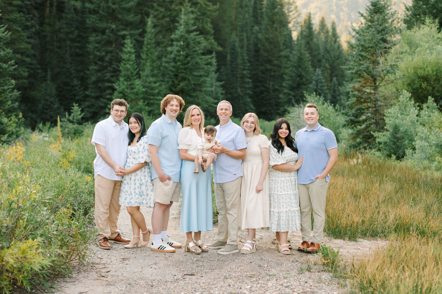 Family of eight posing on a scenic mountain trail surrounded by lush green meadows and pine trees in Utah.