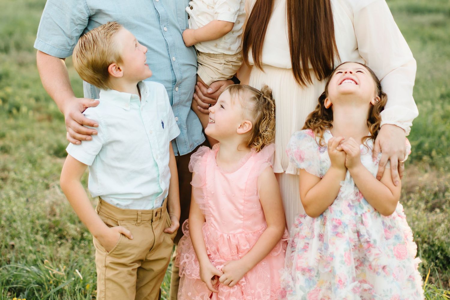 A joyful family with three young children laughing and looking up outdoors in a green field during a portrait session.