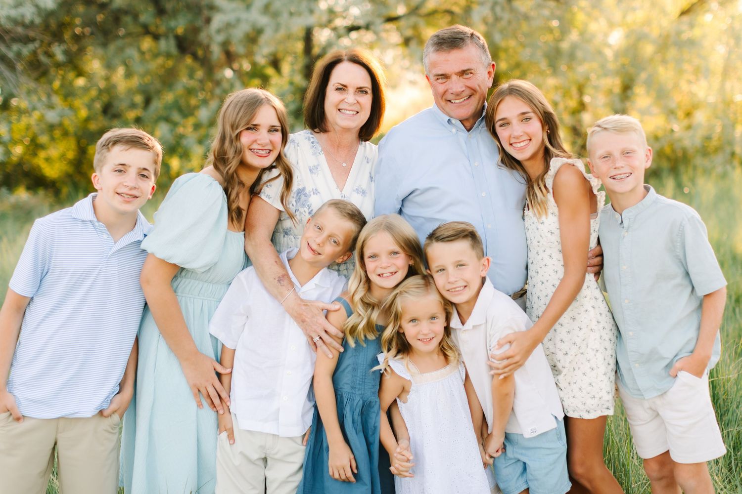 Happy large family portrait with parents and seven children posing outdoors in coordinating blue outfits.