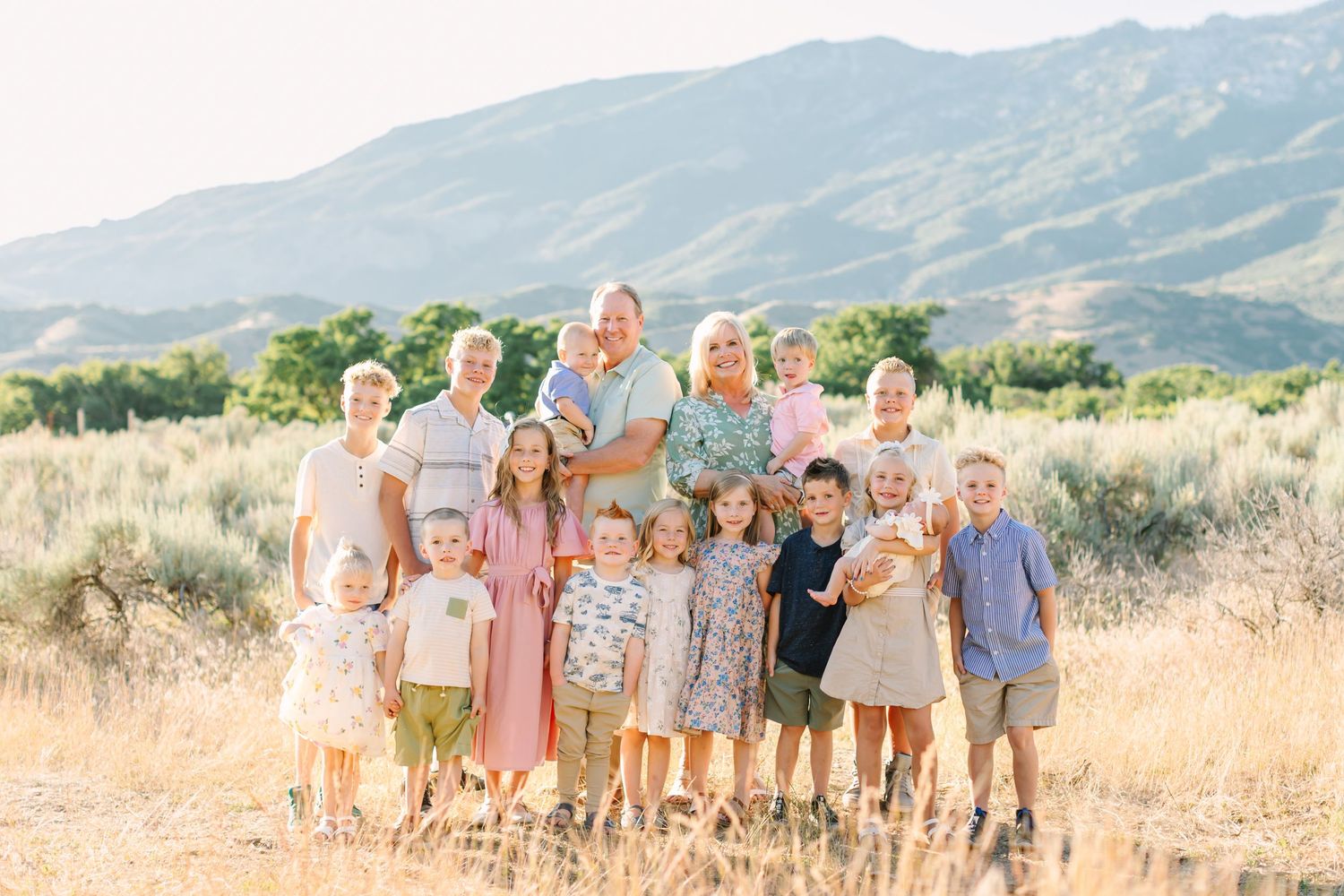 A group poses together in coordinated peach and neutral outfits against a scenic mountain landscape backdrop.