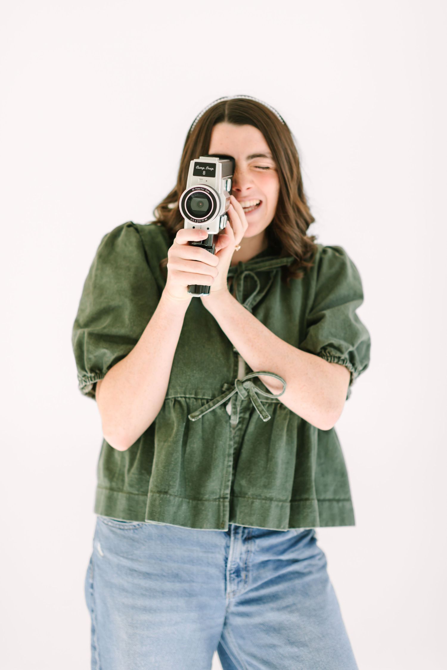 Person in green button-up shirt and jeans holding vintage video camera while filming in studio setting.