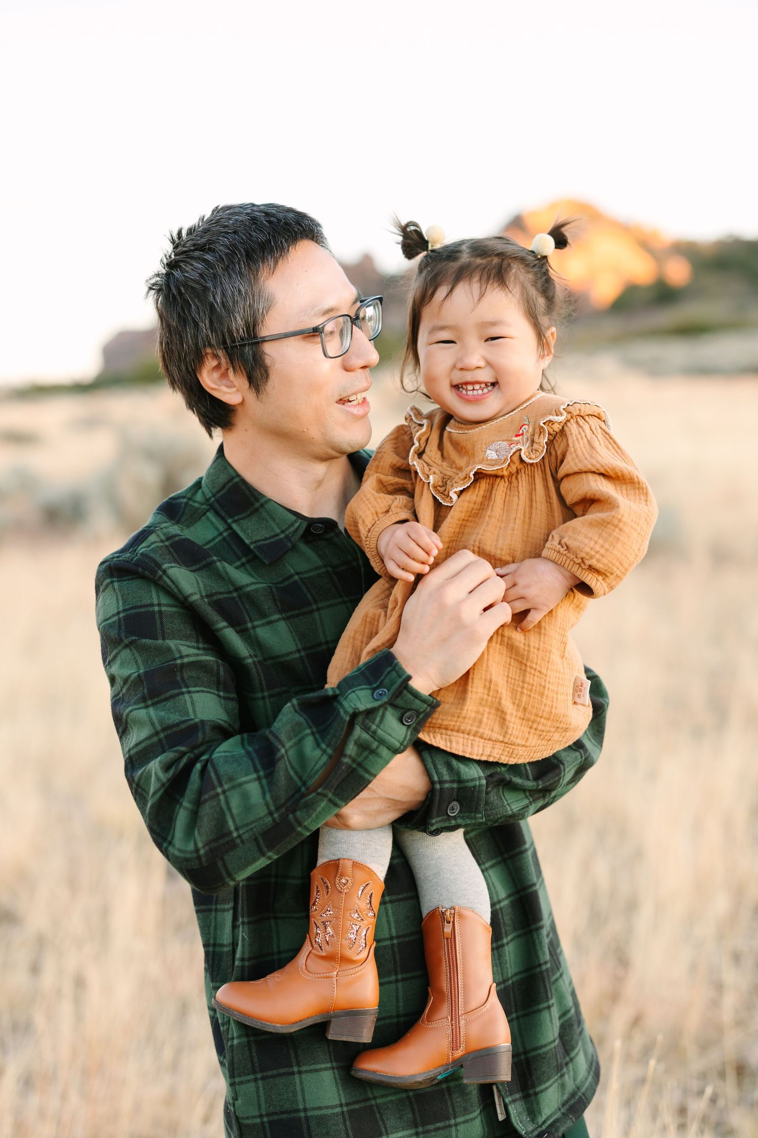 Parent and child share joyful moments together in a field wearing coordinating green plaid and orange sweater outfits.