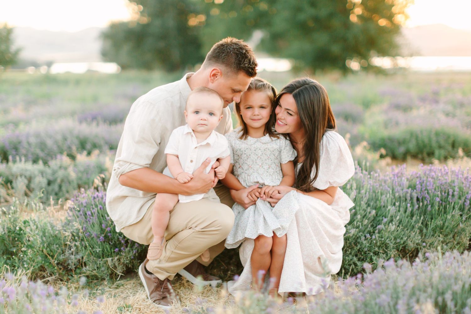 A family wearing white and beige outfits poses together in a blooming lavender field during golden hour.