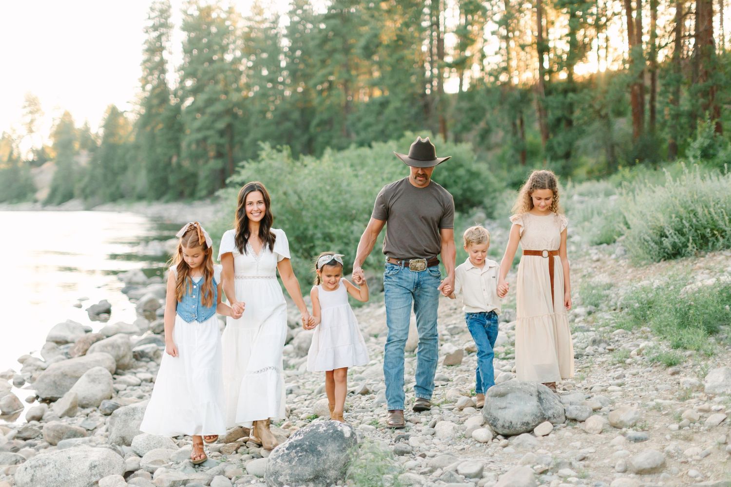 A family walks together along a rocky beach shoreline during golden hour in matching white and denim outfits.
