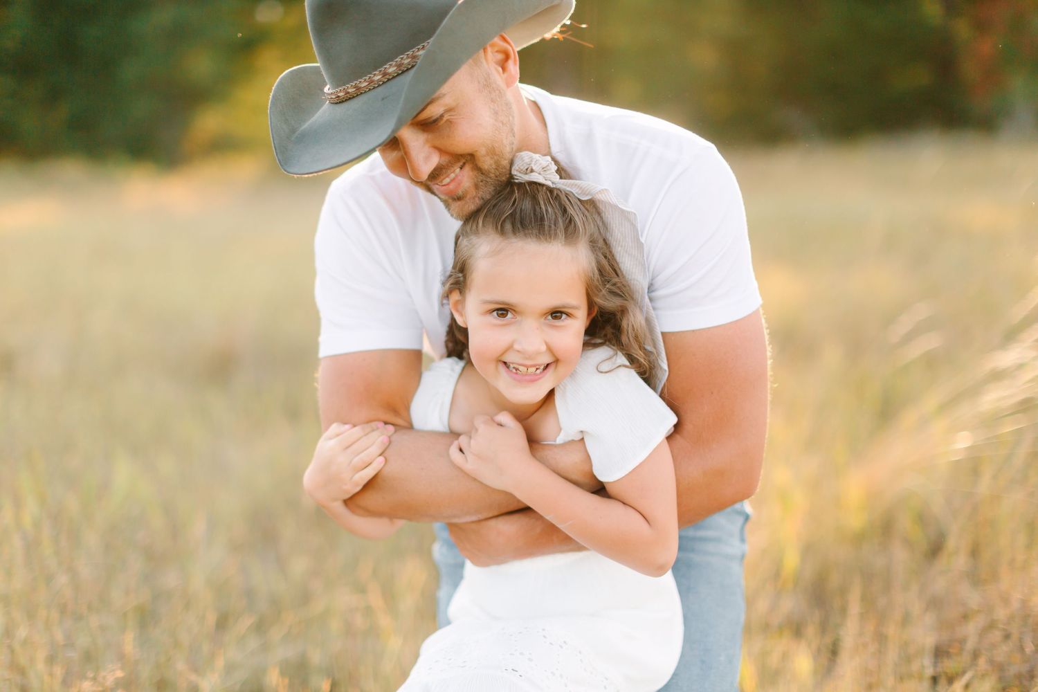 Family embraces in a sunlit meadow wearing white outfits during golden hour photography session.