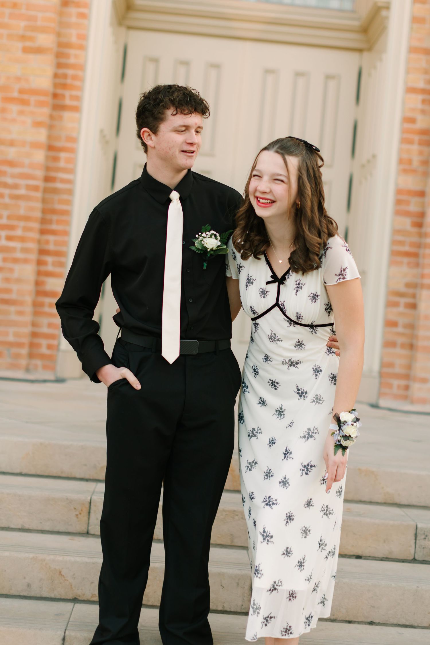 A couple in formal attire poses for three candid photos on stone steps against an orange brick wall.