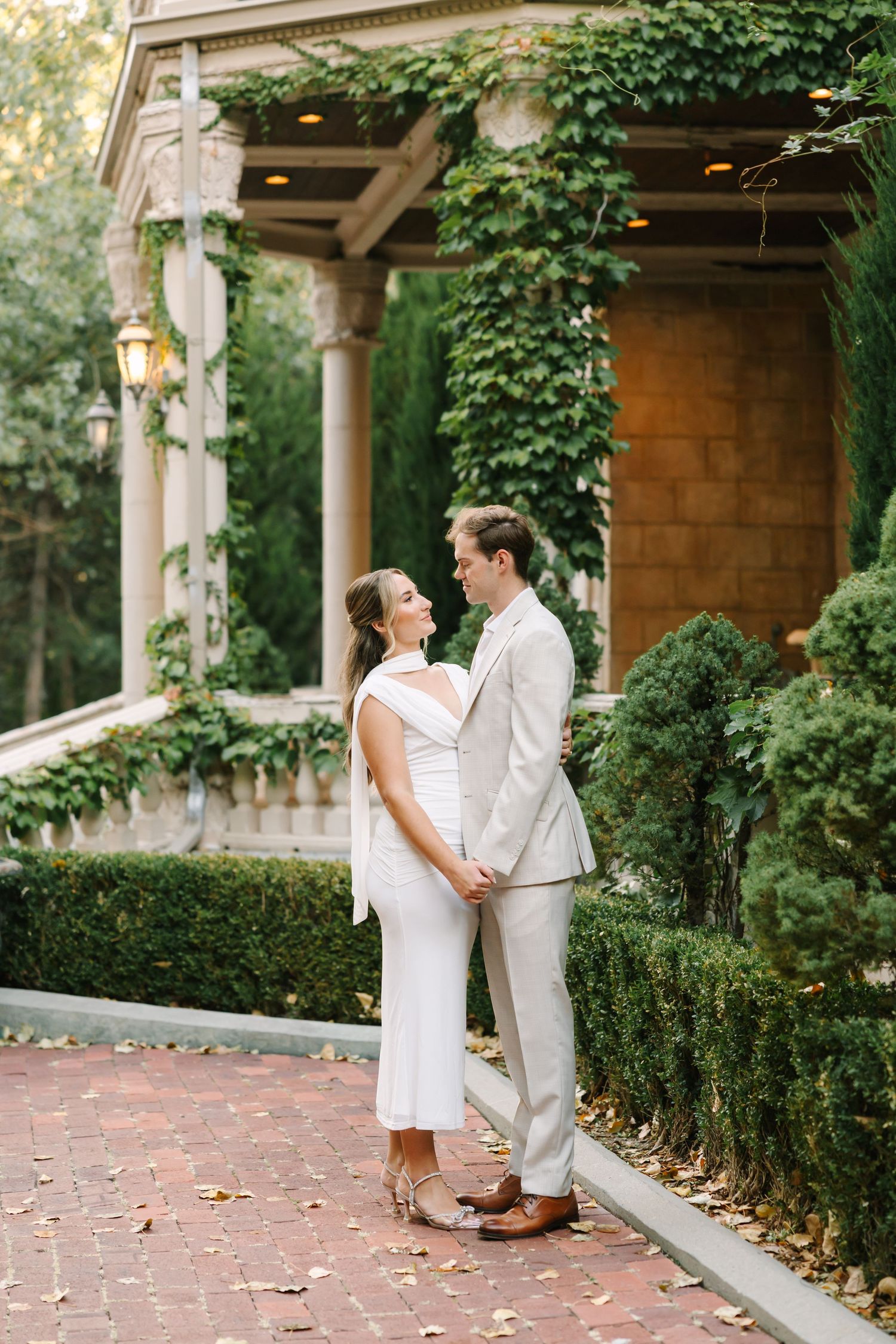Couple shares romantic moments in a garden courtyard with ivy-covered columns and brick pathways.